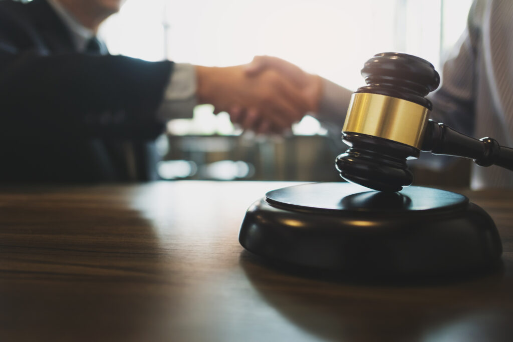 A gavel with a blurred handshake in the background