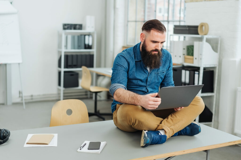 Bearded man sitting on desk with laptop