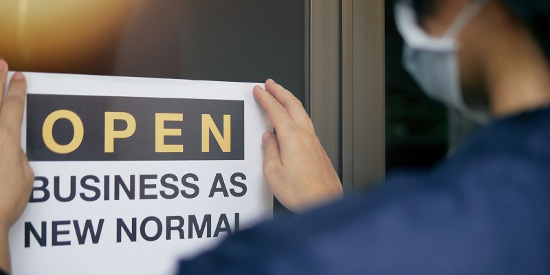 Reopening for business adapt to new normal in the novel Coronavirus COVID-19 pandemic. Rear view of business owner wearing medical mask placing open sign "OPEN BUSINESS AS NEW NORMAL" on front door.