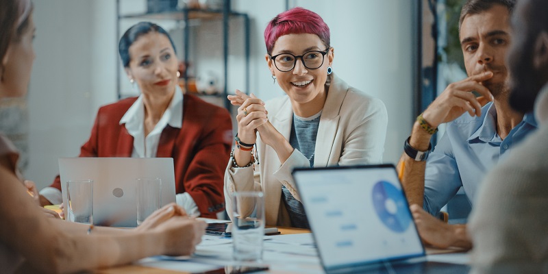 Office Meeting in Conference Room: Beautiful Specialist with Short Pink Hair Talks about Firm Strategy with Diverse Team of Professional Businesspeople. Creative Start-up Team Discusses Big Project